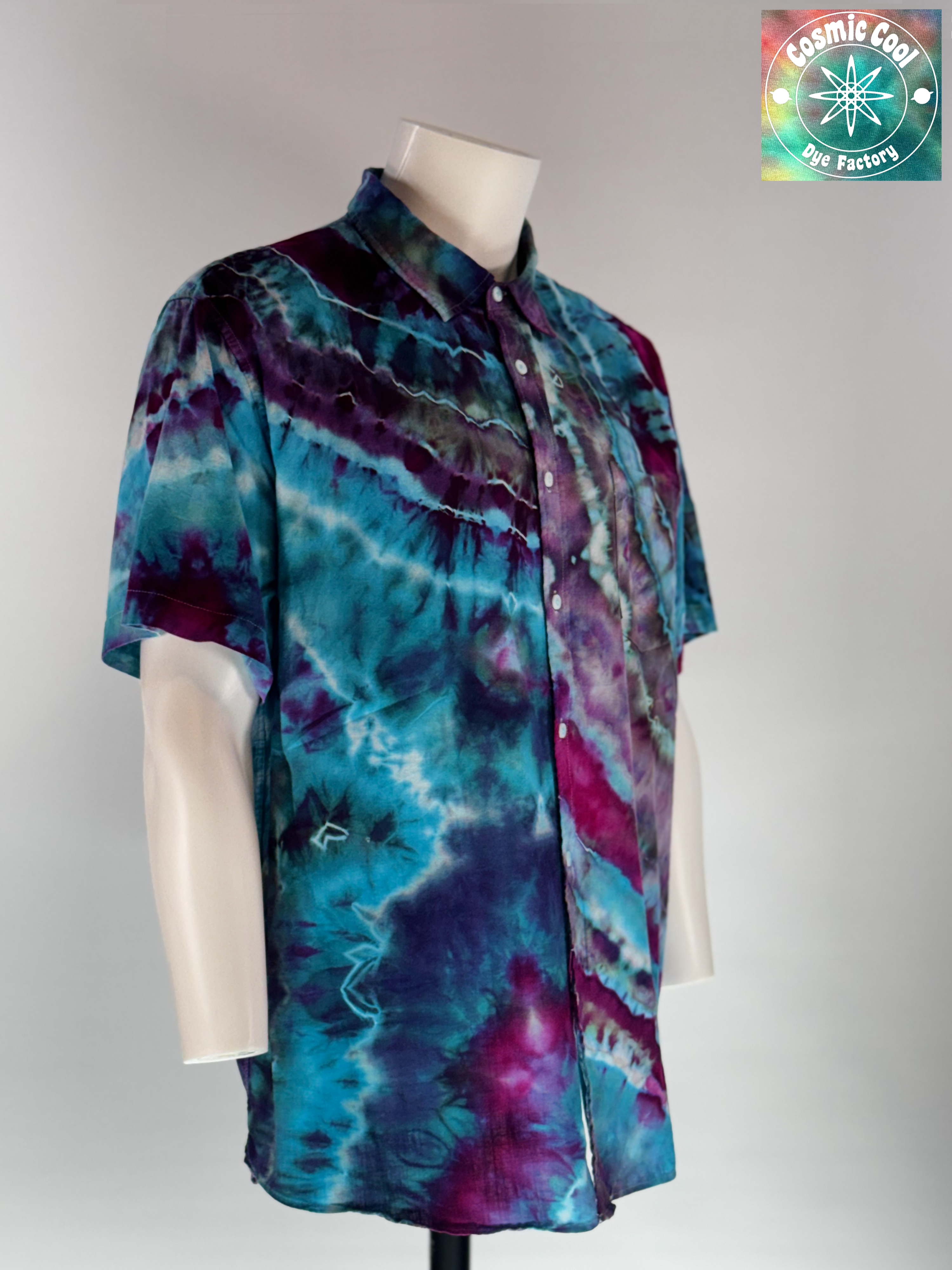 Angled 3/4 Front view of our Cosmic Camp Shirt. Geodesic tides mimics the rhythmic, mineral-like layering found in coastal geodes. The design features a cascading flow of deep amethyst and royal purple waves that wash over a vibrant turquoise and teal base.