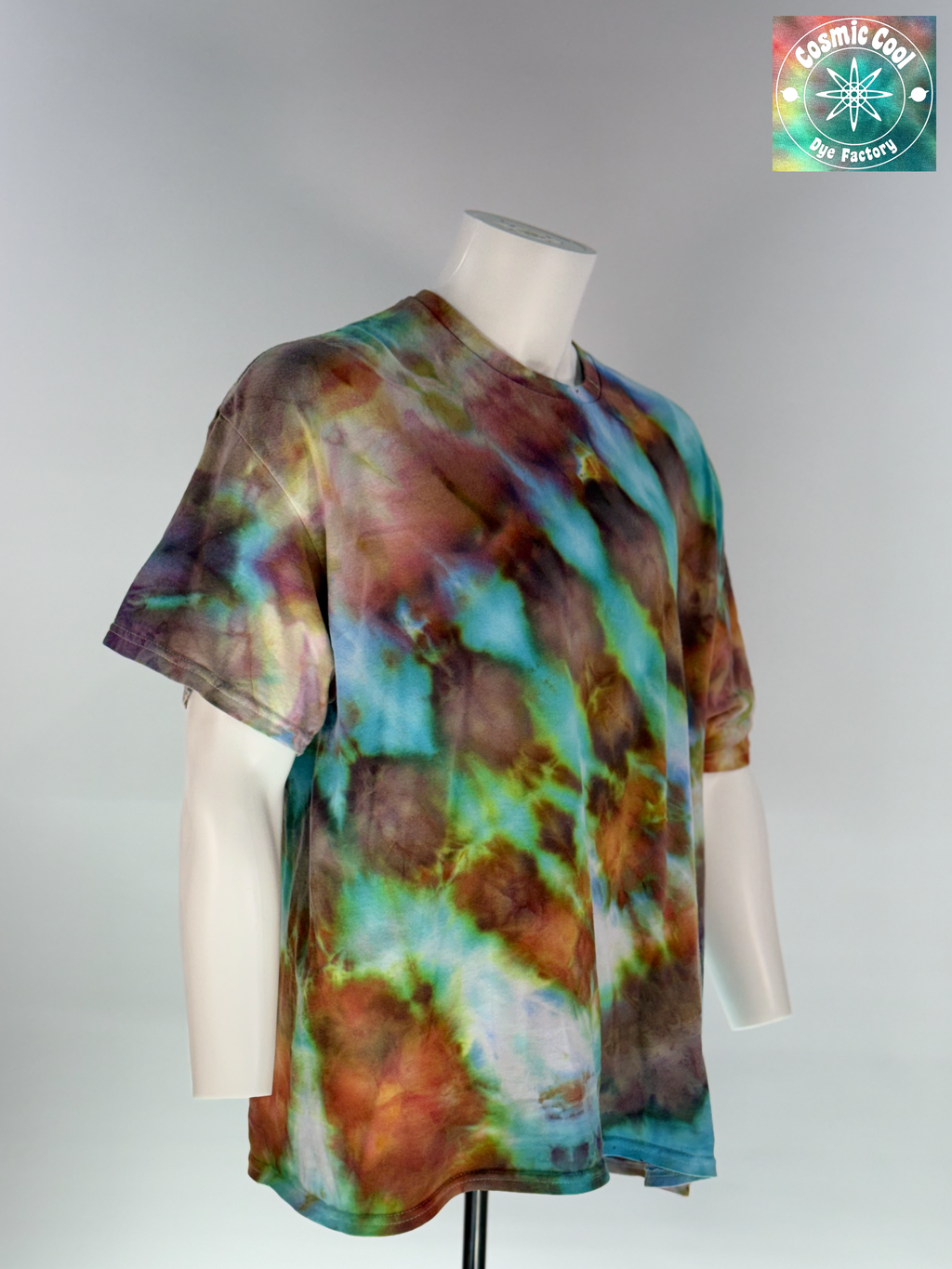 Angled 3/4 Front view of a 2XL Short Sleeve Artisan Tee. Phoenix Elixir features a high-energy, diagonal flow of color. The design is dominated by radiant teals and ethereal sky blues that are "invaded" by scorched earth umbers and molten copper highlights. These colors meld to create a shimmering, liquid effect