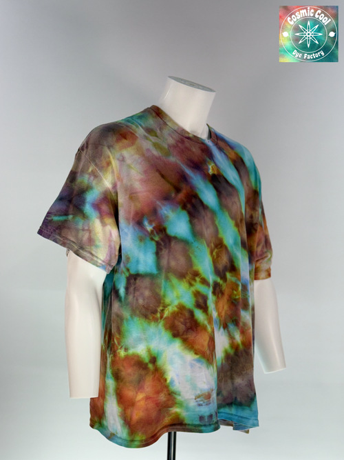Angled 3/4 Front view of a 2XL Short Sleeve Artisan Tee. Phoenix Elixir features a high-energy, diagonal flow of color. The design is dominated by radiant teals and ethereal sky blues that are "invaded" by scorched earth umbers and molten copper highlights. These colors meld to create a shimmering, liquid effect