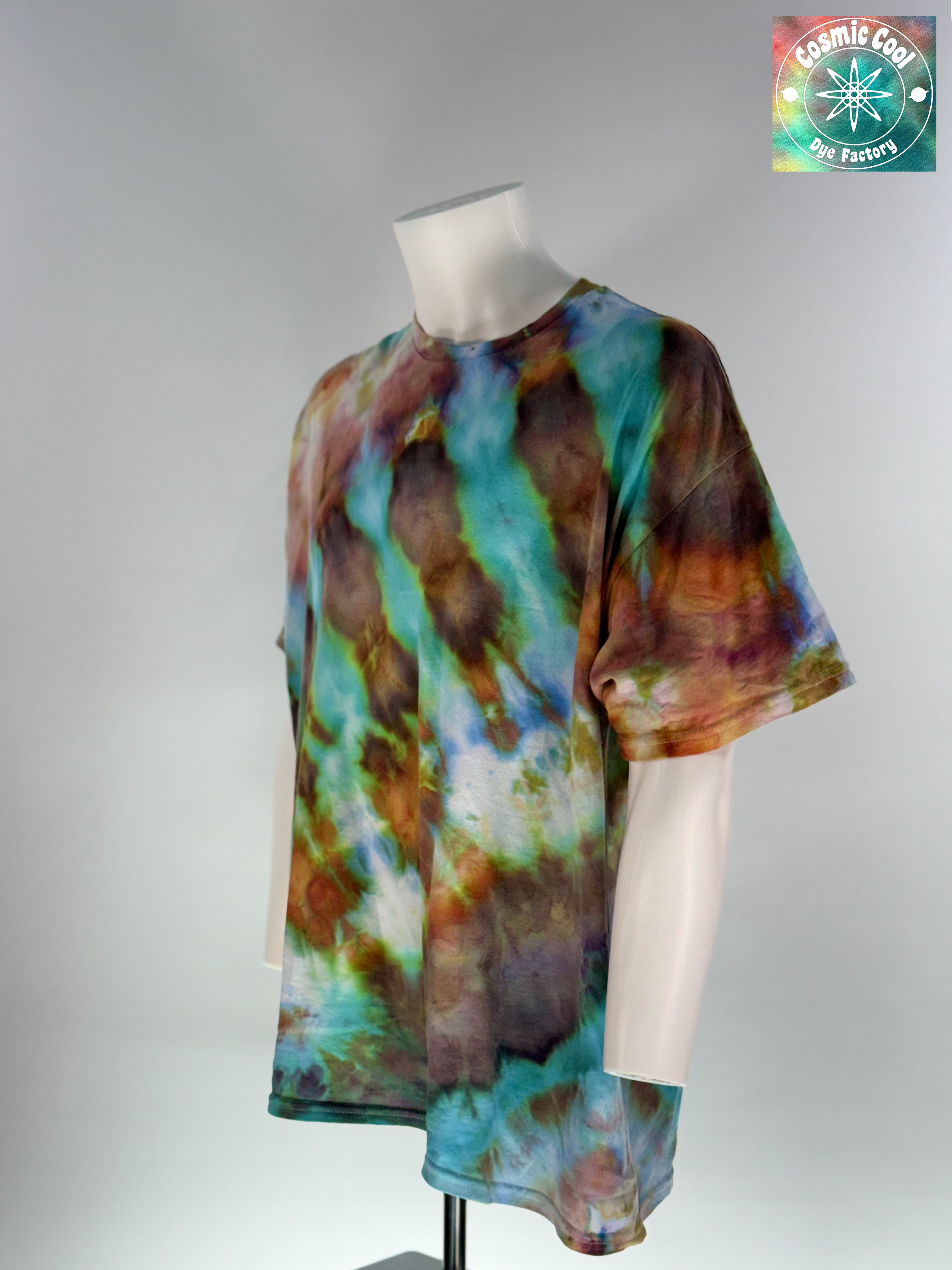 Angled 3/4 Front view of a 2XL Short Sleeve Artisan Tee. Phoenix Elixir features a high-energy, diagonal flow of color. The design is dominated by radiant teals and ethereal sky blues that are "invaded" by scorched earth umbers and molten copper highlights. These colors meld to create a shimmering, liquid effect