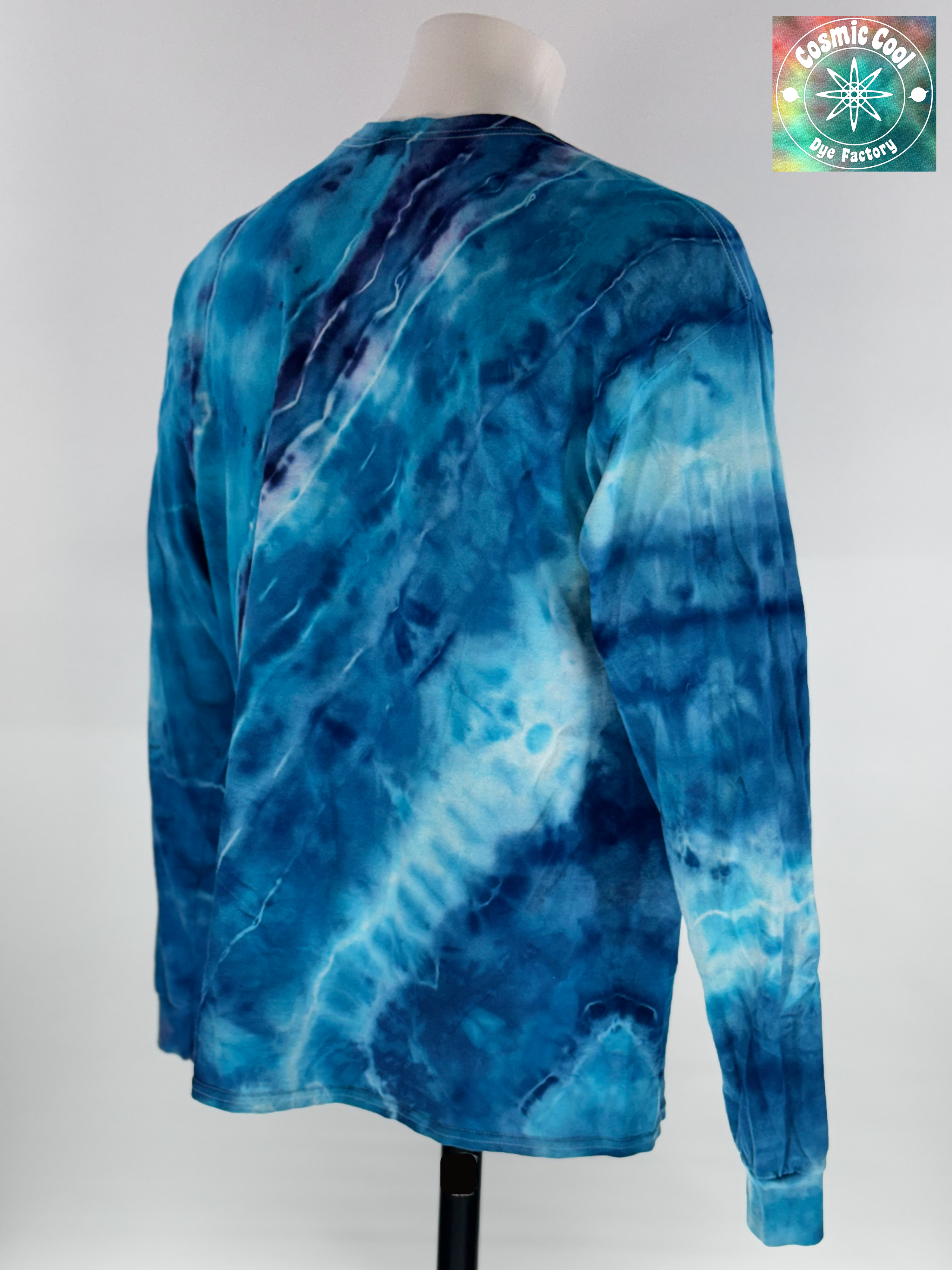 Angled 3/4 back view of XL Long Sleeve Ice Dyed Tee Shirt. Glacier Horizon is defined by a deep, diagonal "Tectonic Rift" of competing blues. Navy, Glacier, Cerulean, and Midnight blue that all leave their  Radiant "ice shelves" of turquoise and electric cerulean, creating a complex fracturing of color that mimics ancient, shifting ice. 