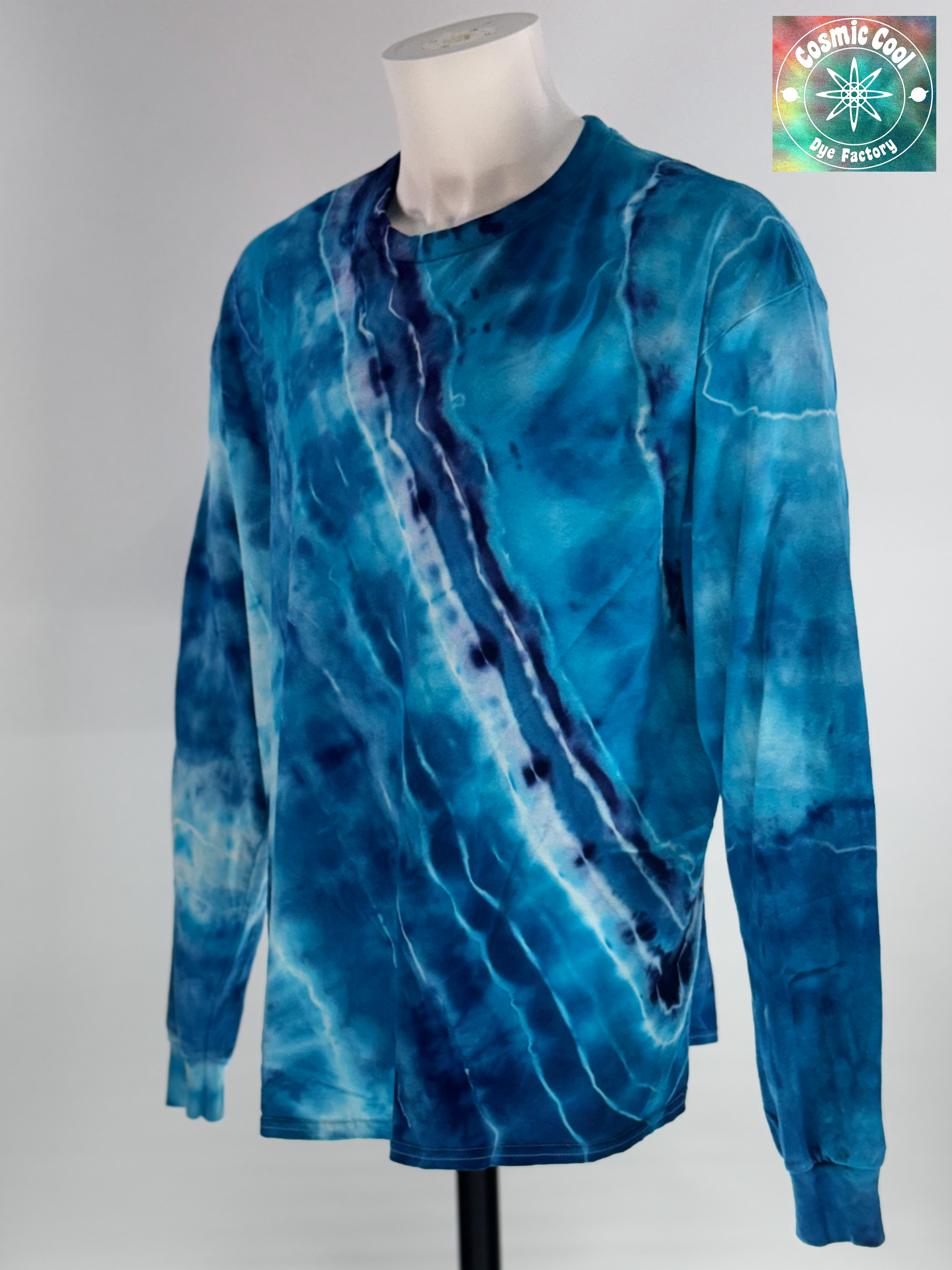 Angled 3/4 Front view of XL Long Sleeve Ice Dyed Tee Shirt. Glacier Horizon is defined by a deep, diagonal "Tectonic Rift" of competing blues. Navy, Glacier, Cerulean, and Midnight blue that all leave their  Radiant "ice shelves" of turquoise and electric cerulean, creating a complex fracturing of color that mimics ancient, shifting ice. 
